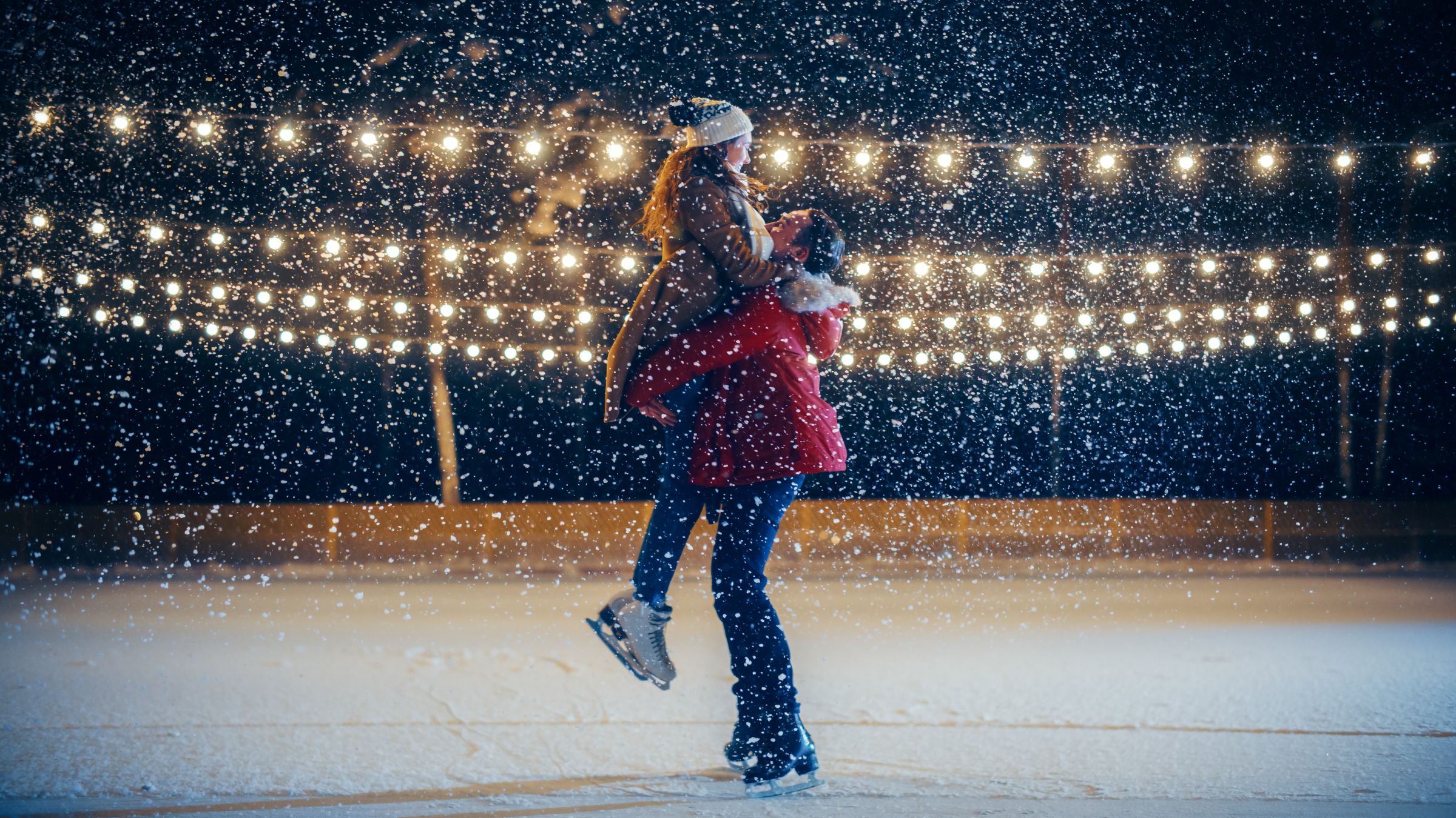 Couple embracing on skating rink under christmas lights